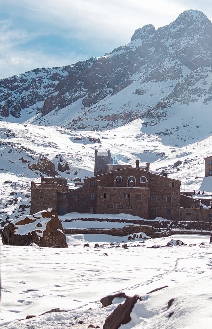 Panorama of Nangma Valley campsite with river flowing by backed by huge craggy mountains with snow
